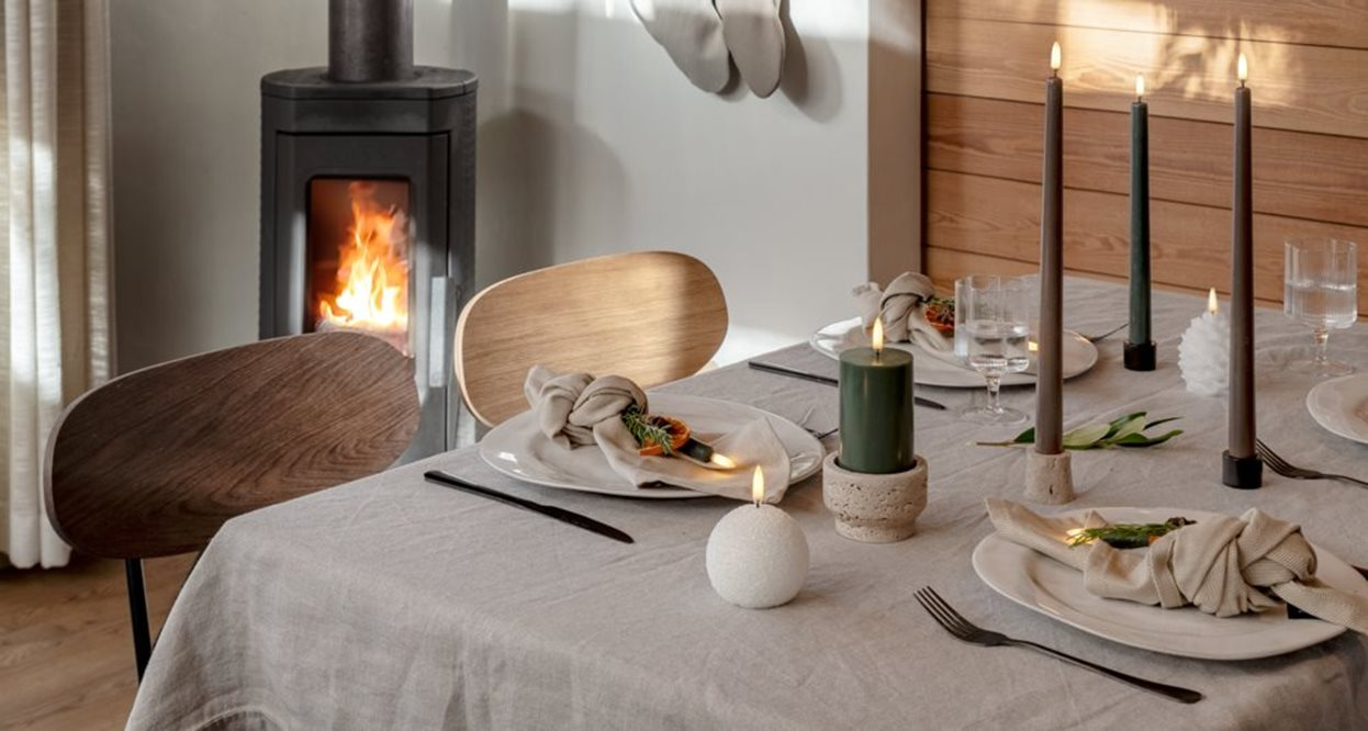 Dining table set with candles and plates in a cozy room with a fireplace.