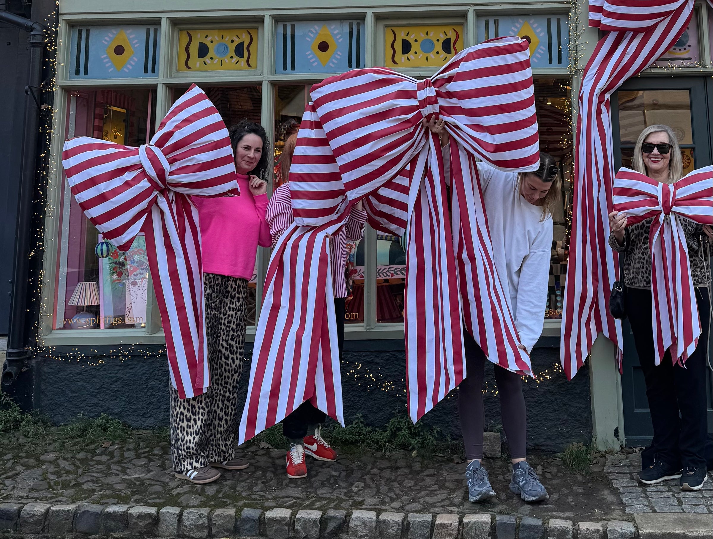 People holding large red and white striped bows in front of a store window.
