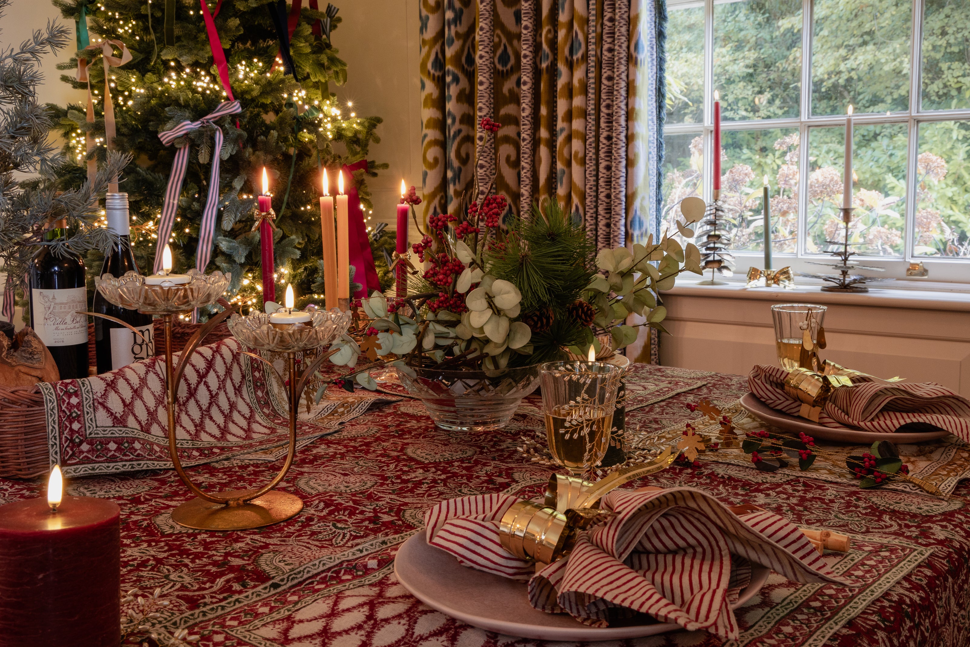 Decorated table with Christmas tree, candles, and flowers in a cozy room.