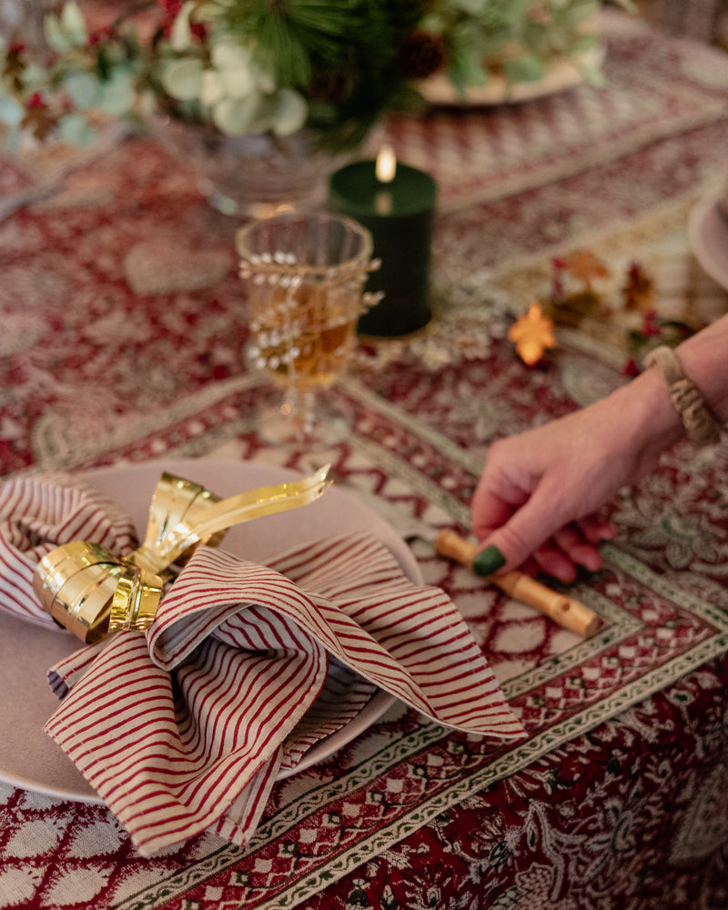 Decorative table setting with striped napkin and gold napkin ring on a patterned tablecloth.