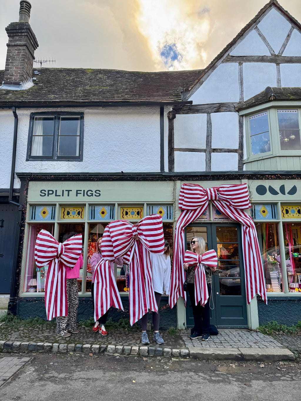 People wearing large red and white striped bows in front of a building with 'Split Figs' sign.