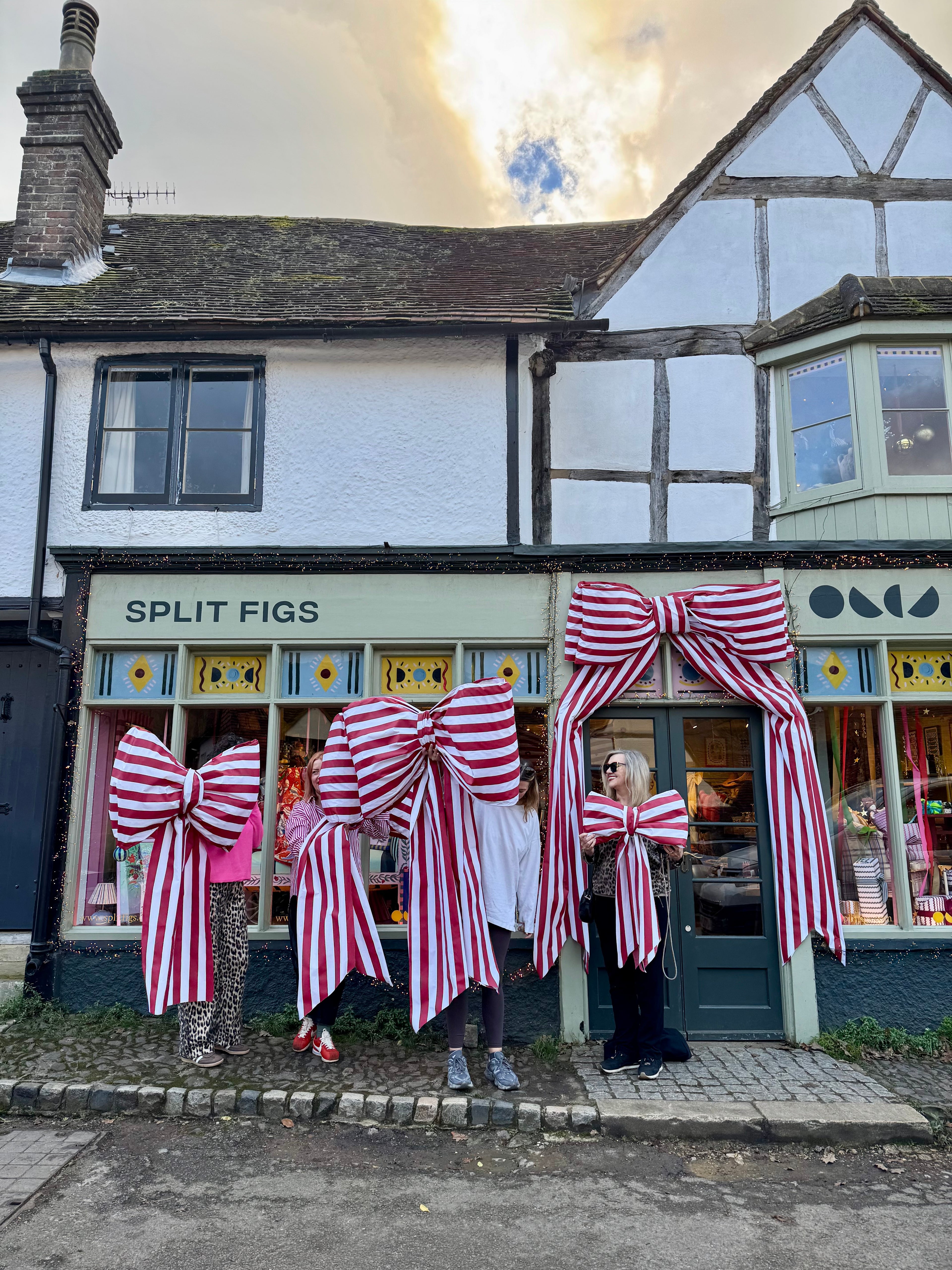 People wearing large red and white striped bows in front of a building with 'Split Figs' sign.